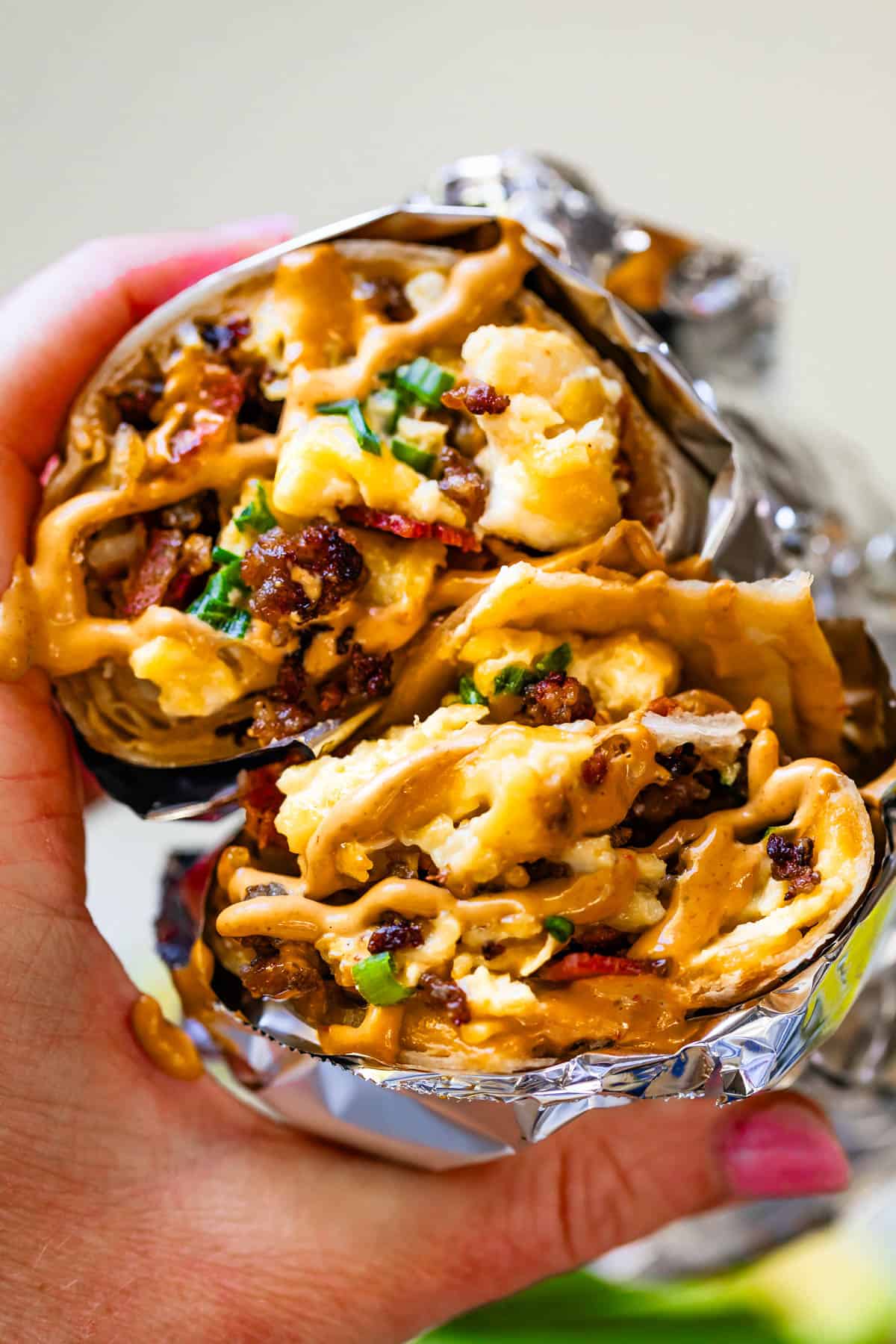 Two breakfast burrito wrapped in foil with sauce on top with bites taken out.