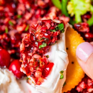 Cranberry Cream cheese dip on a Ritz cracker held up in someone's hand.