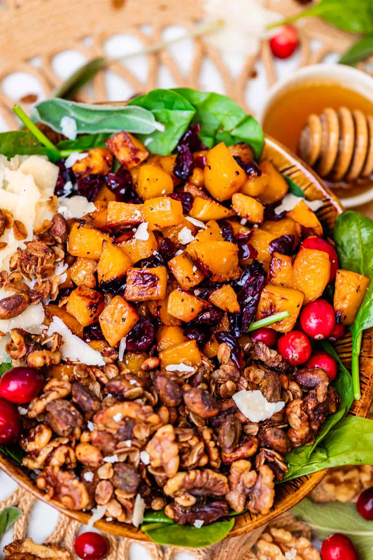 bowl of honey roasted butternut squash salad sitting on a counter with a bowl of honey behind it.