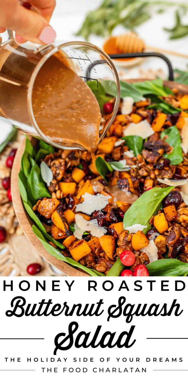pouring dressing over a butternut squash and spinach salad in a wooden bowl with black handles.
