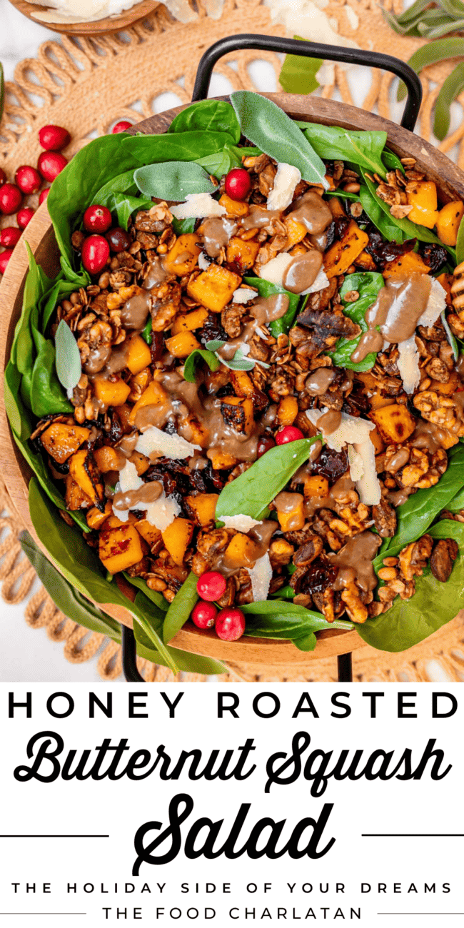 a big salad in a wooden bowl with balck handles, with spinach, squash, parmesan, dressing, and cranberries.