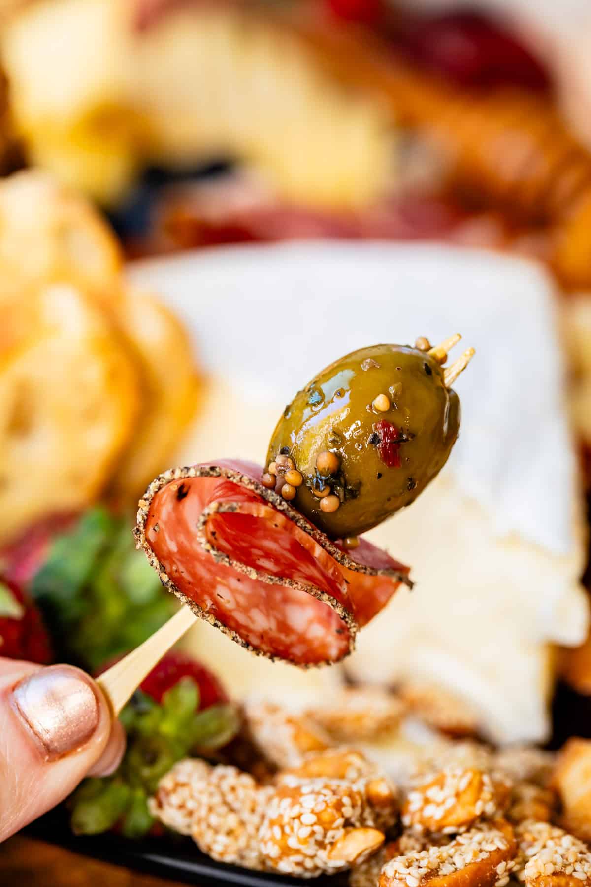 Bite of black pepper salami and green olive on toothpick from charcuterie board.