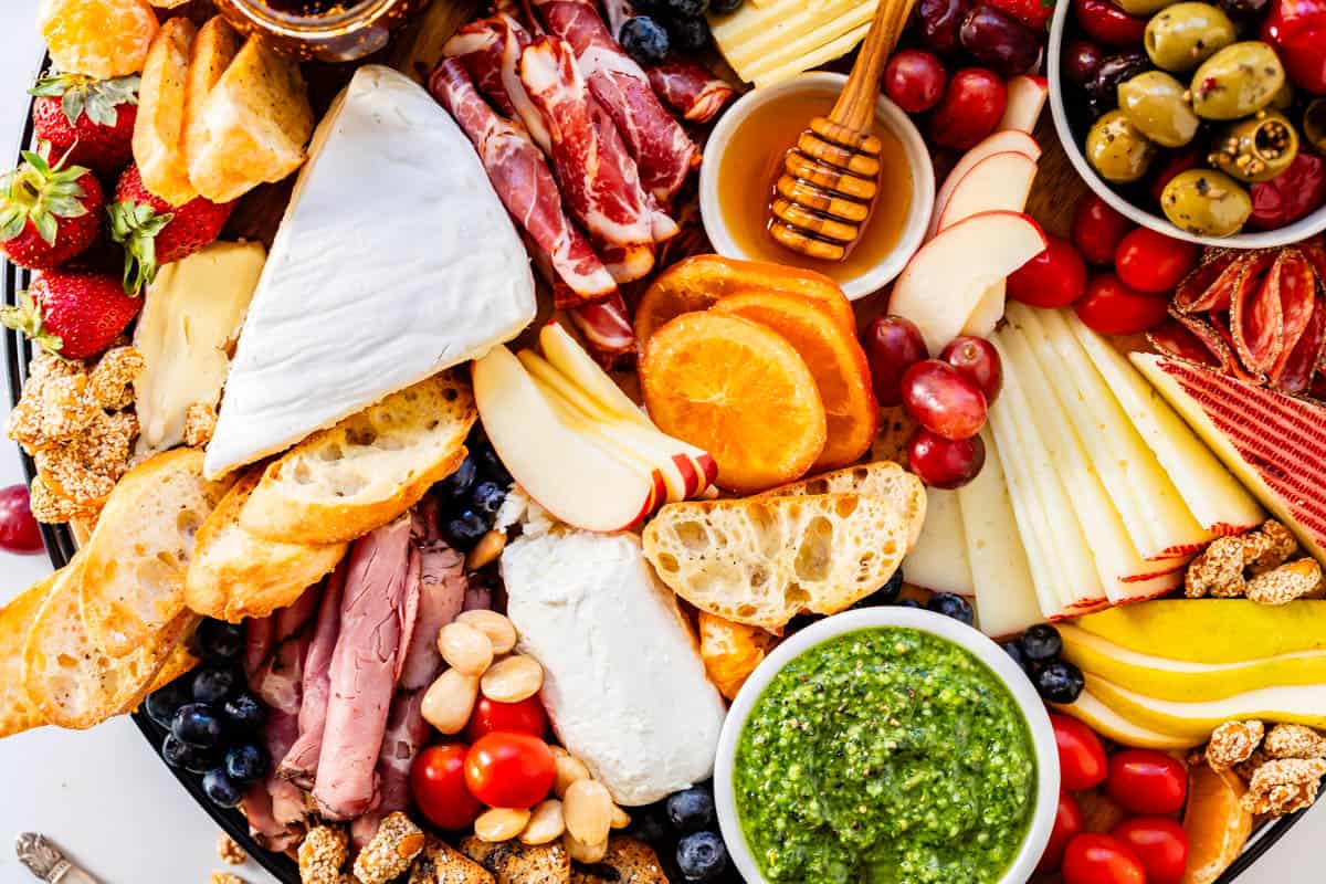 Charcuterie board arranged with assortment of cheese, fruit, meats, nuts, sauces, spreads, bread, and crackers.
