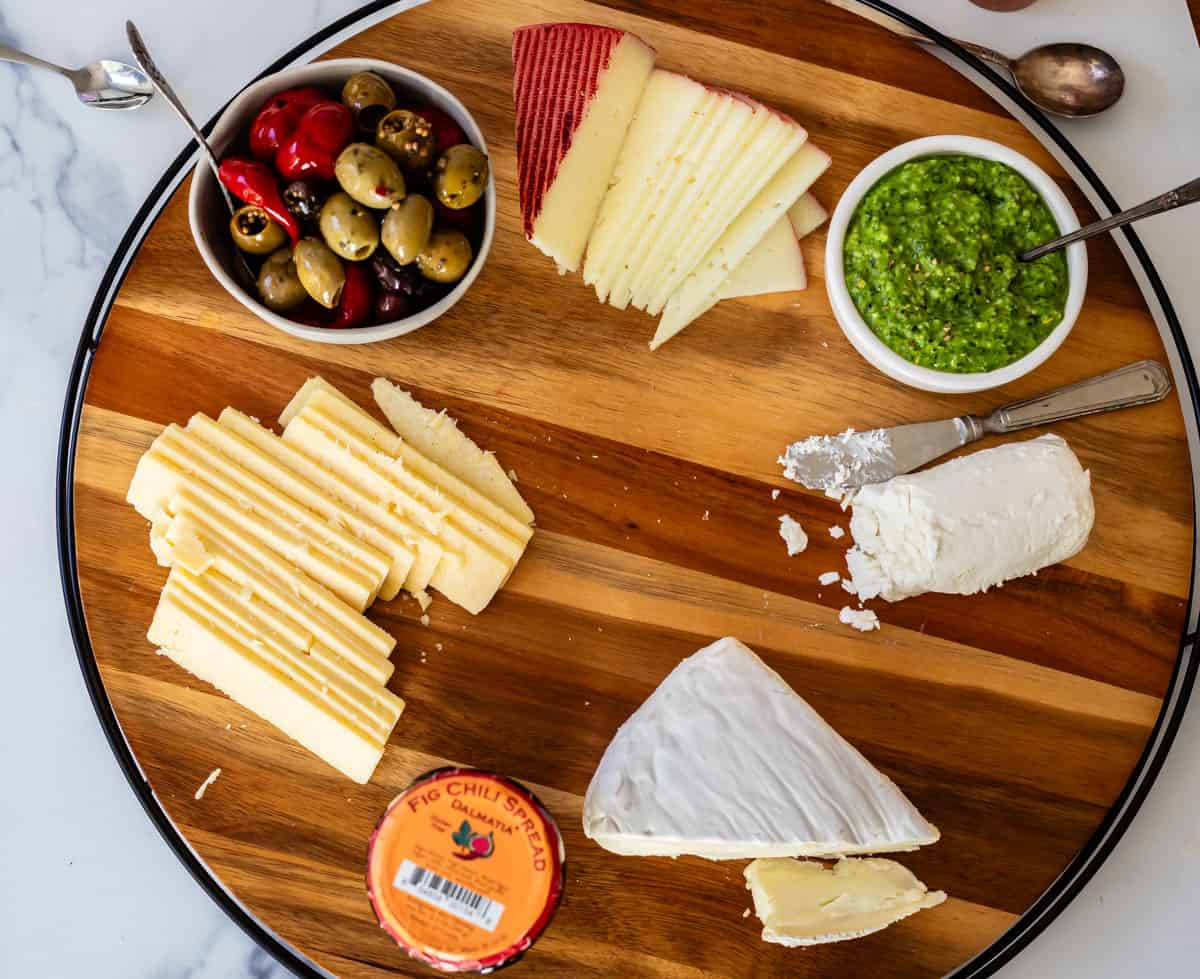 Arranging charcuterie board with cheeses, sauces, and olives in the first part of assembling the display.