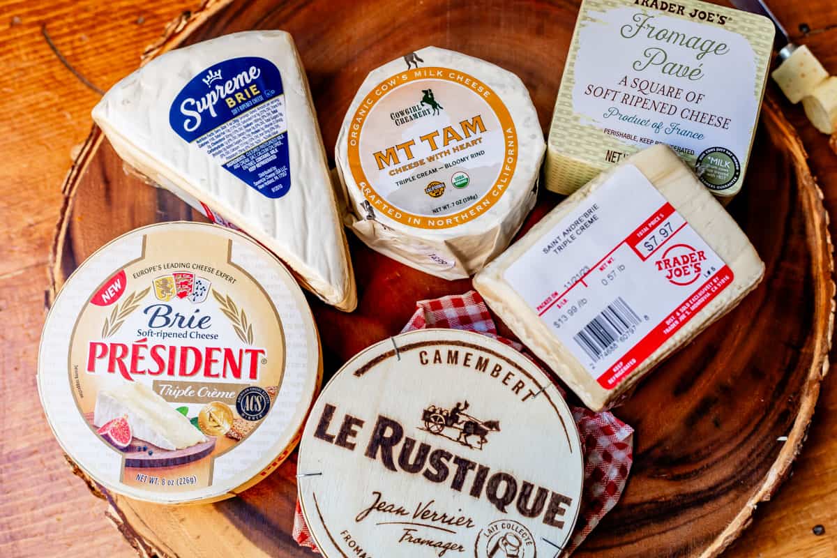 Assortment of nice triple cream cheeses in packaging arranged on a wooden display board.