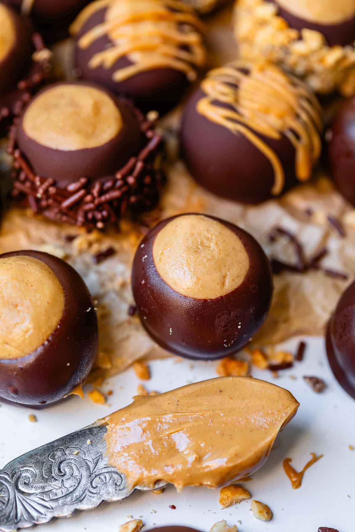 buckeye balls lined up on parchment paper, with a butter knife with peanut butter on it.