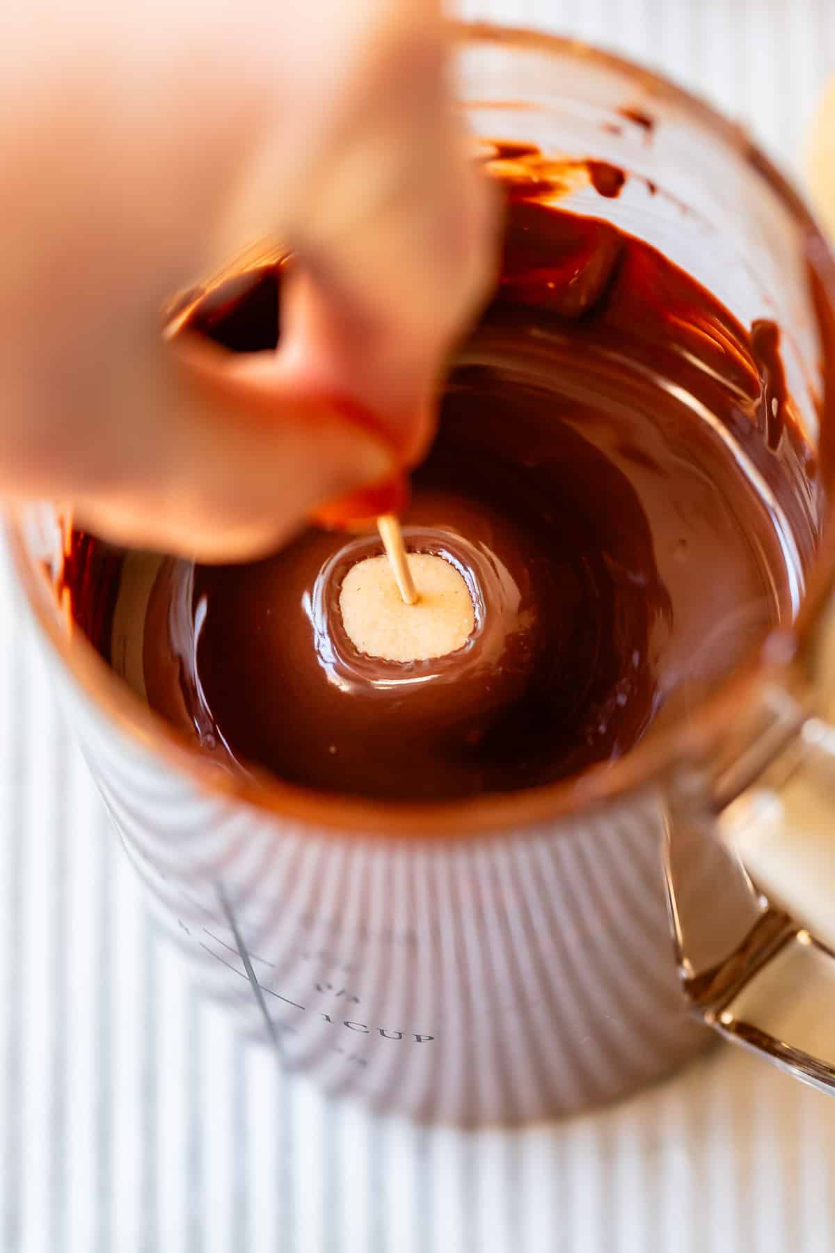a hand dipping peanut butter dough ball into melted chocolate to make buckeyes.