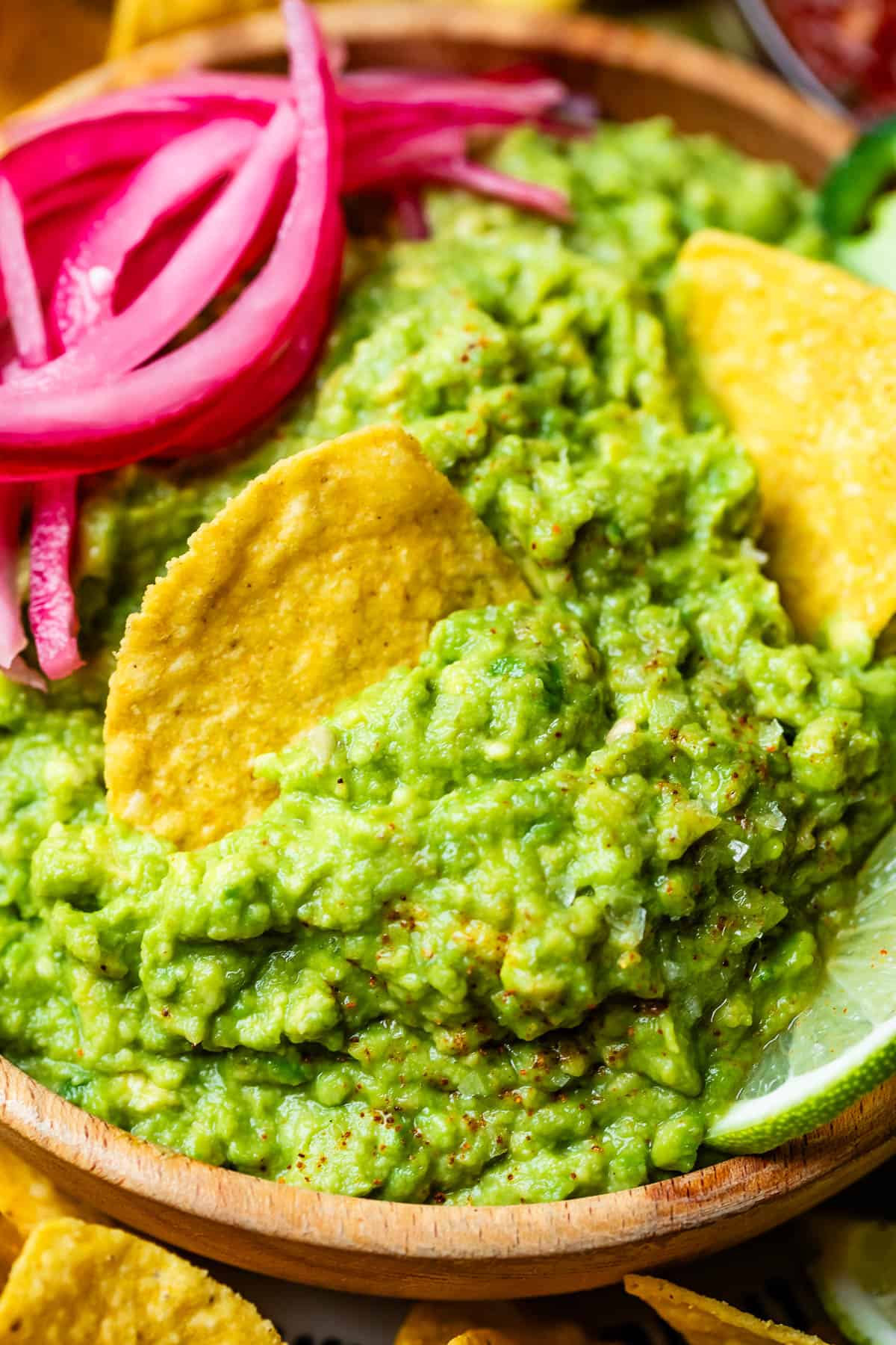 looking down on a guacamole bowl with red onion as a garnish and a chip scooping some out.