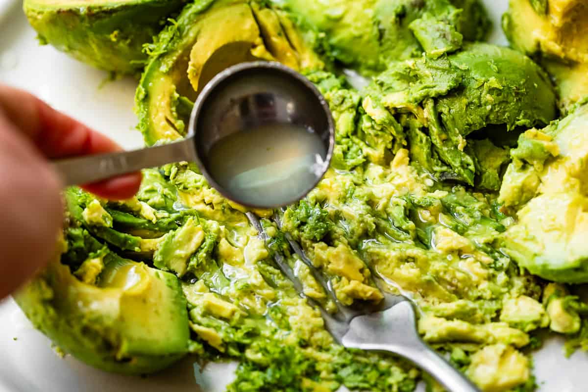 tablespoon adding lime juice over the avocados on a plate as they are being smashed.