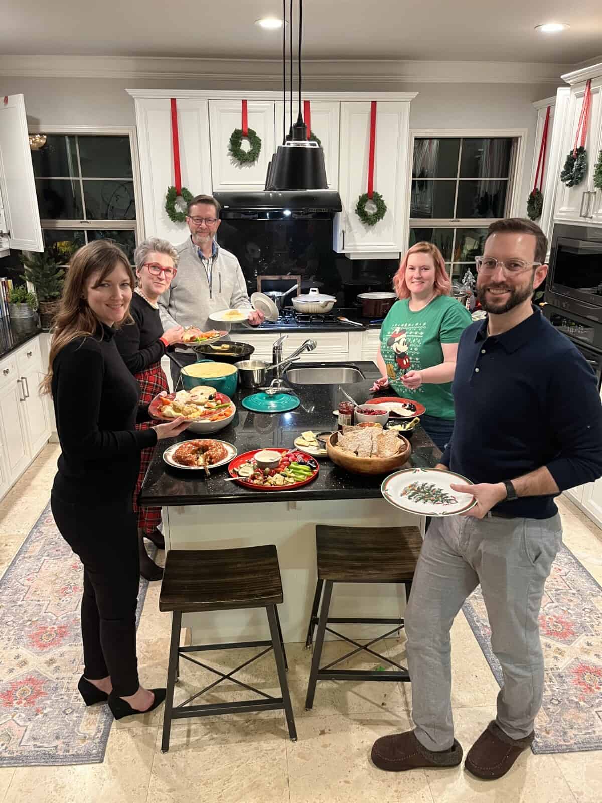 family around a kitchen eating a buffet of food.