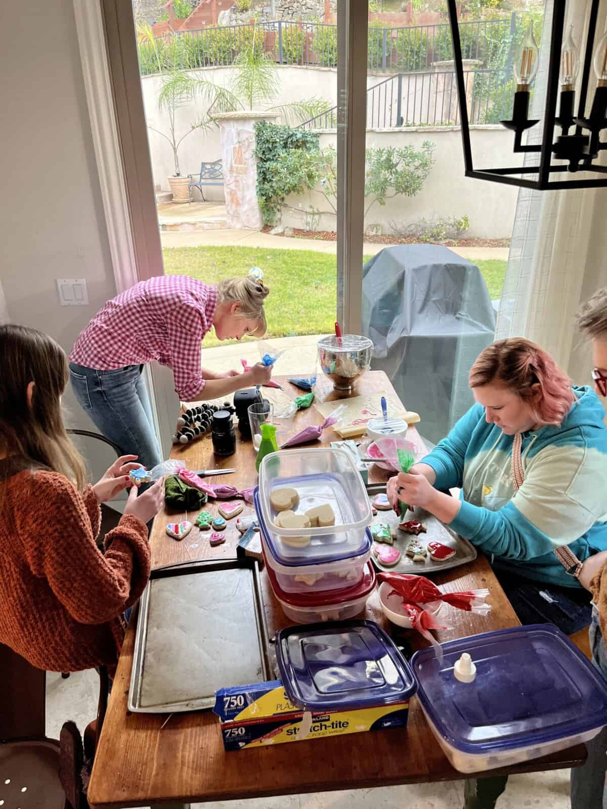 women around a wood table decorating cookies.