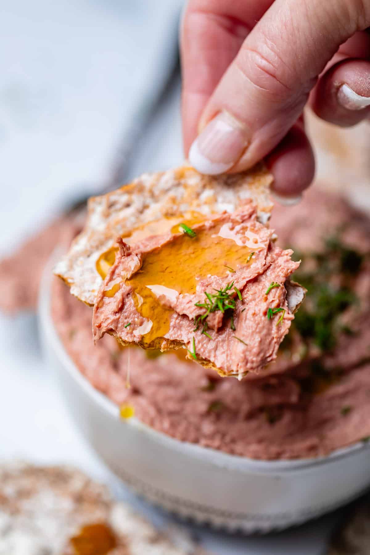 Piece of flatbread covered in liver pate with olive oil and dill drizzled on top.