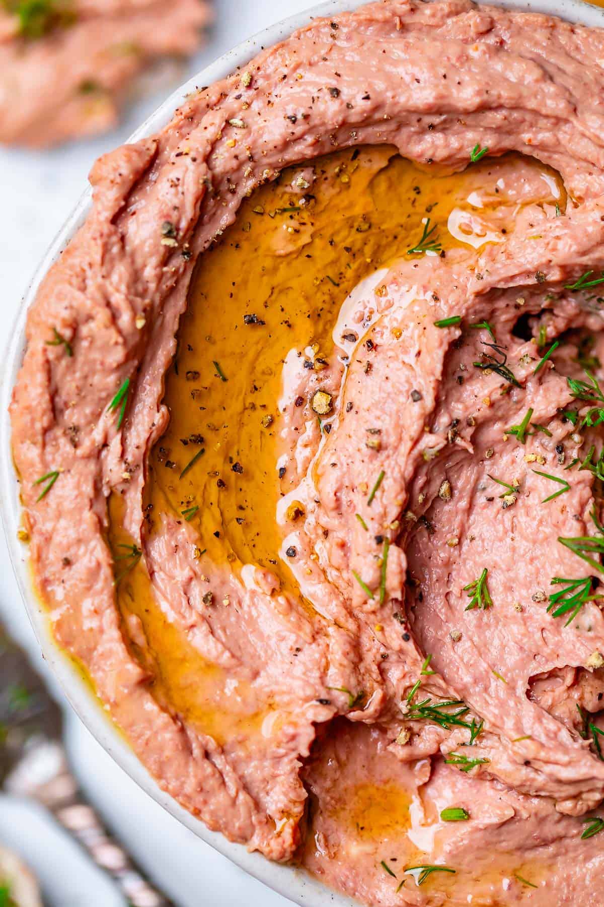 Liver pate in bowl with spices including salt, cracked pepper, and dill with olive oil drizzled on top.