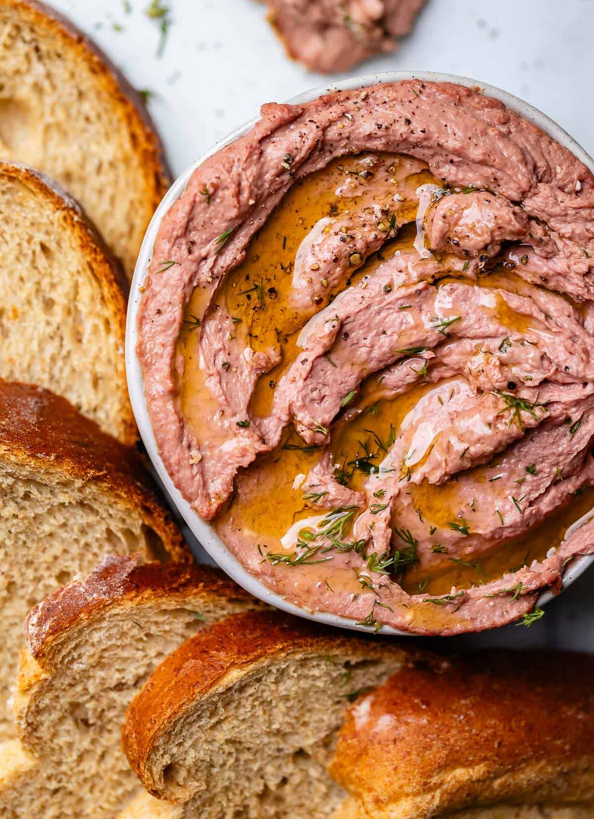 Liver pate in bowl surrounded by slices of rye bread.