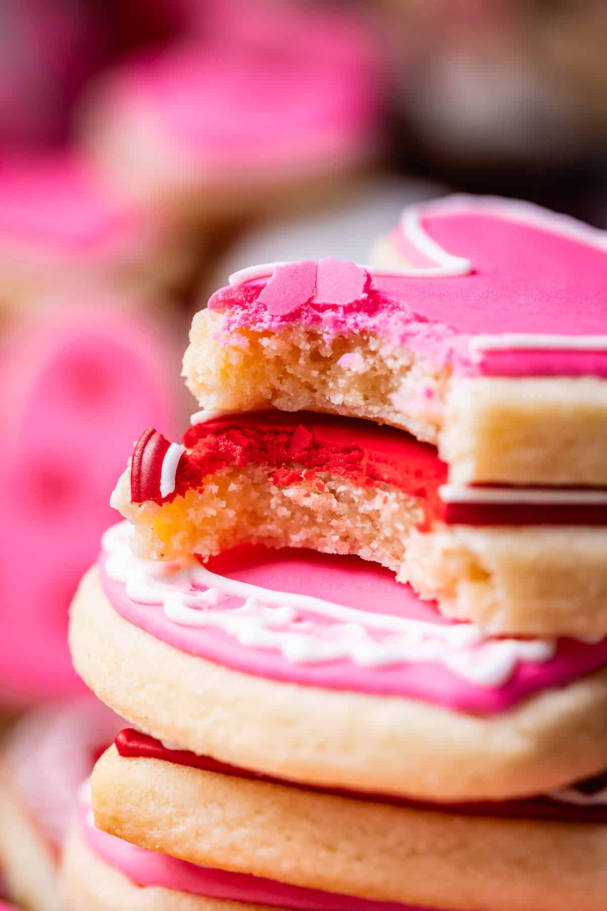 bite taken out of two red and pink sugar cookies, frosted with royal icing.