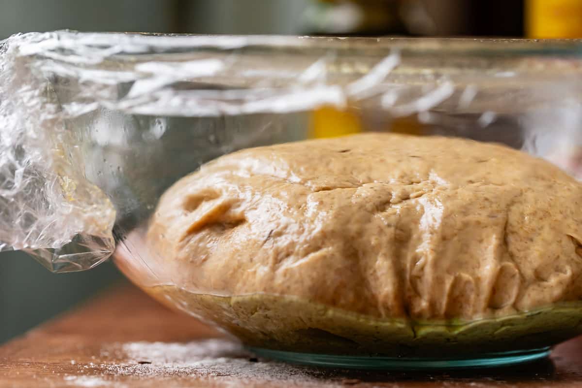 ball of dough in an oiled glass bowl, covered in plastic wrap to rise.