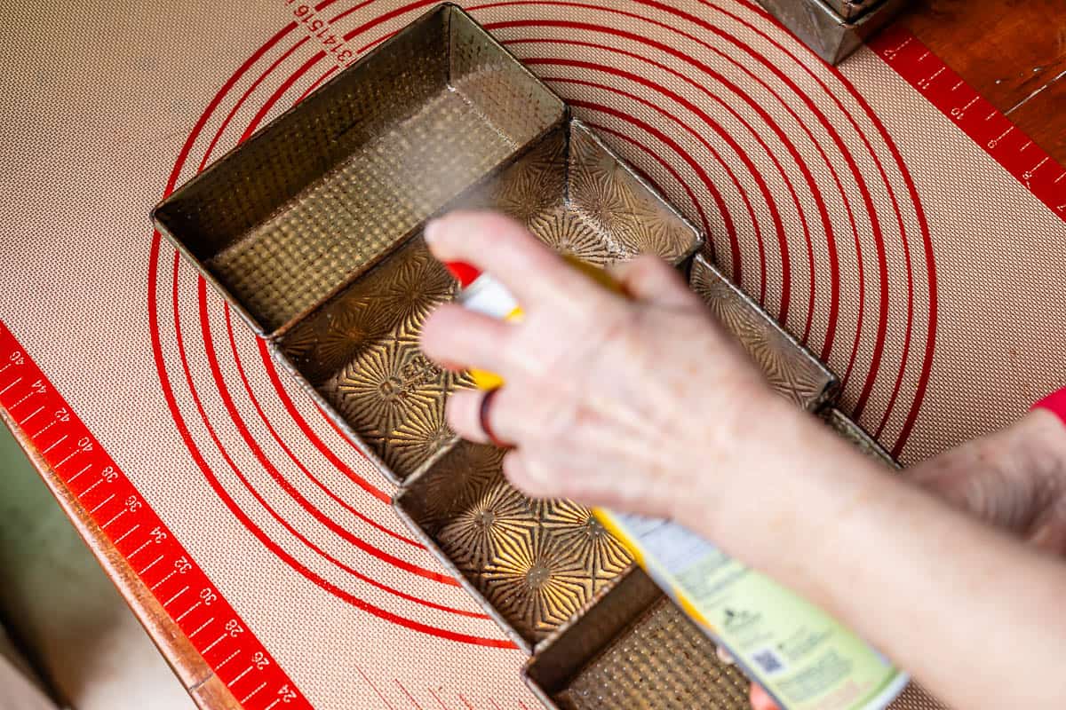Four 7x4 inch loaf pans being sprayed with nonstick cooking spray.