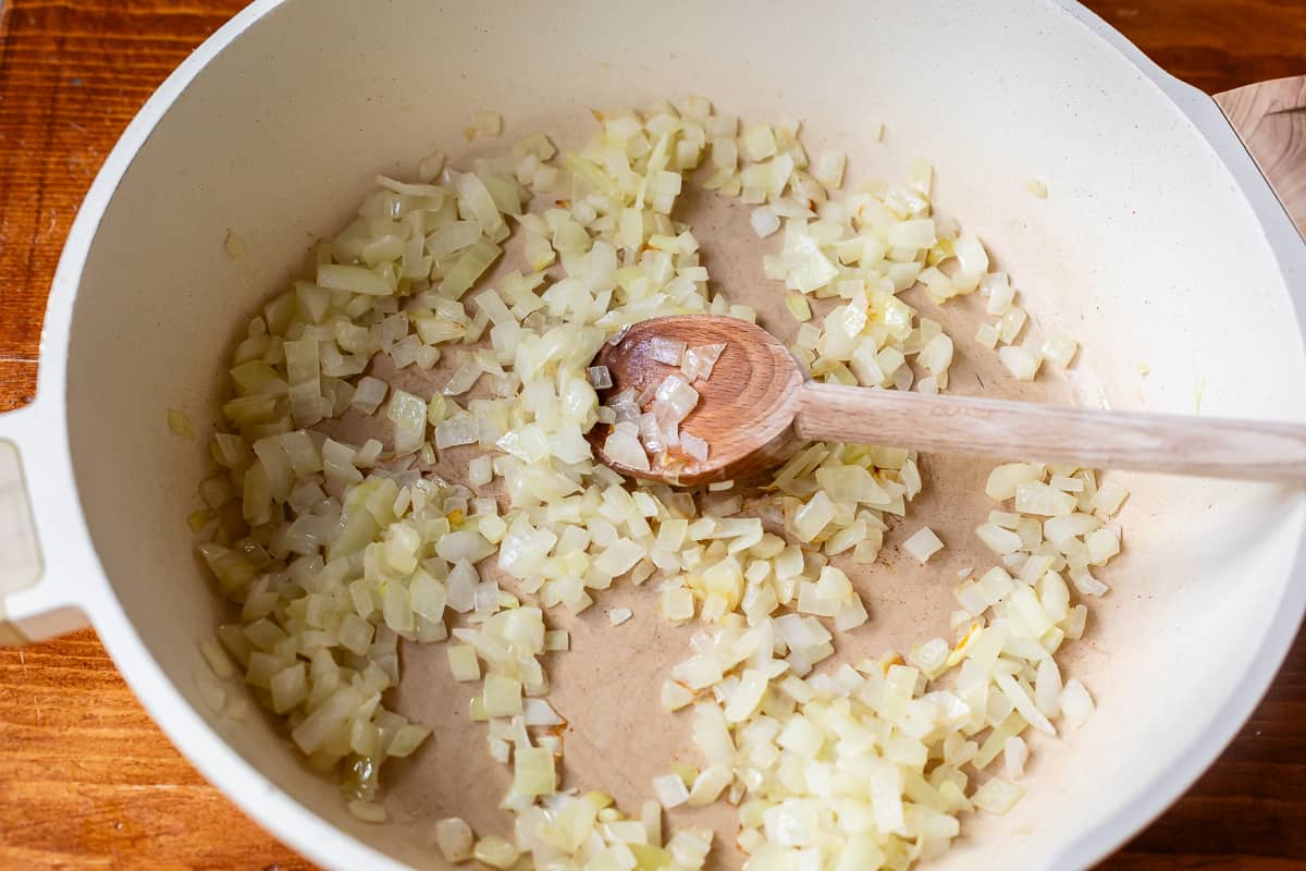 chopped onions sautéing in a large skillet being stirred by a wooden spoon.