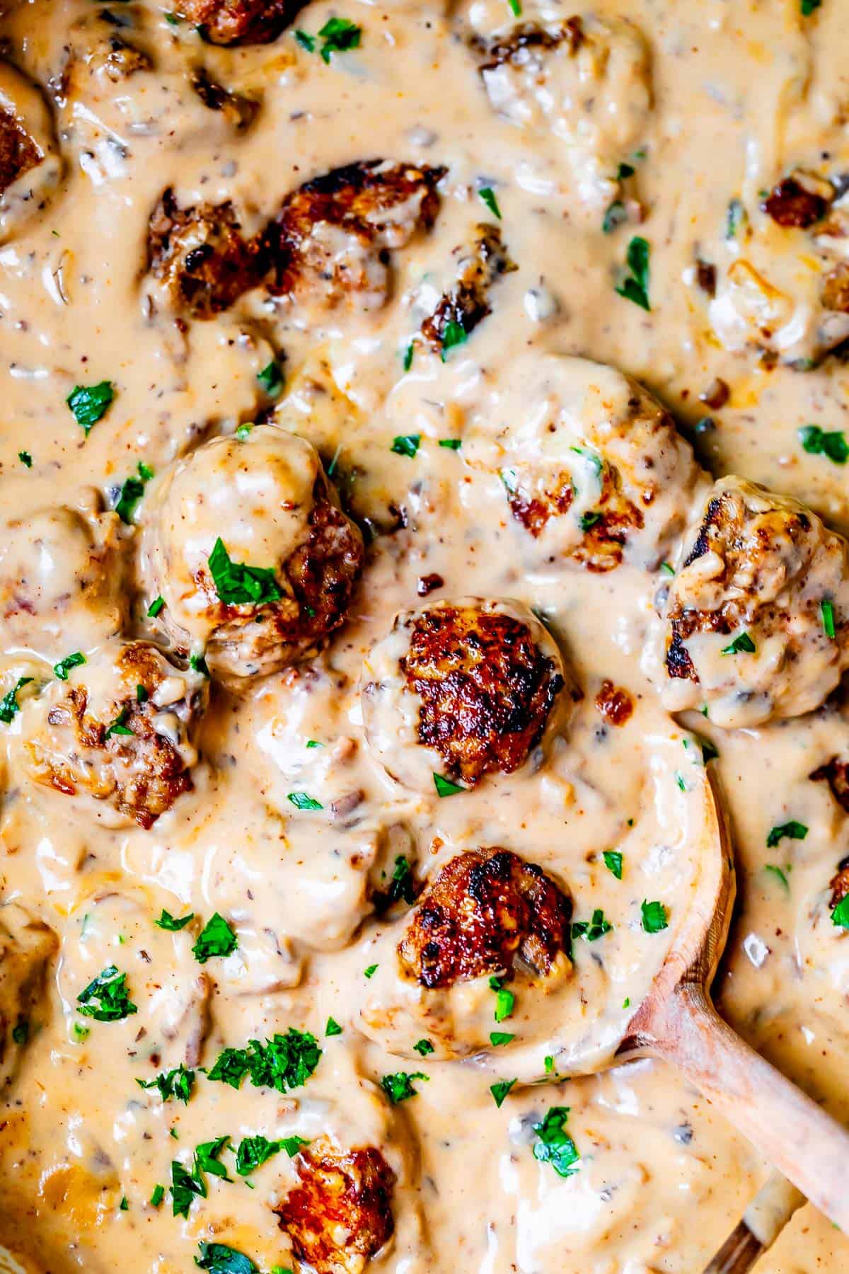 a large wooden spoon stirring together swedish meatballs and creamy gravy.