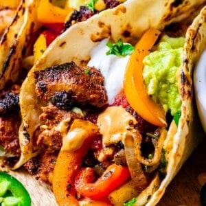 close up of chicken fajitas in tortilla with peppers and onions, sour cream, cilantro.
