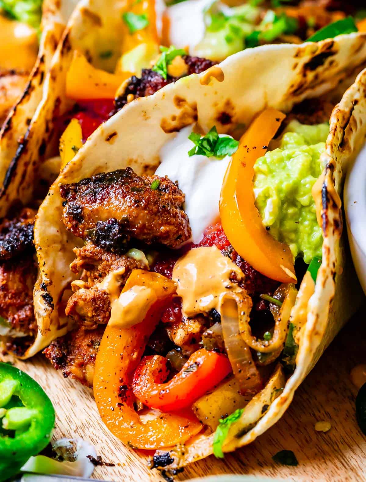 close up of chicken fajitas in tortilla with peppers and onions, sour cream, cilantro.