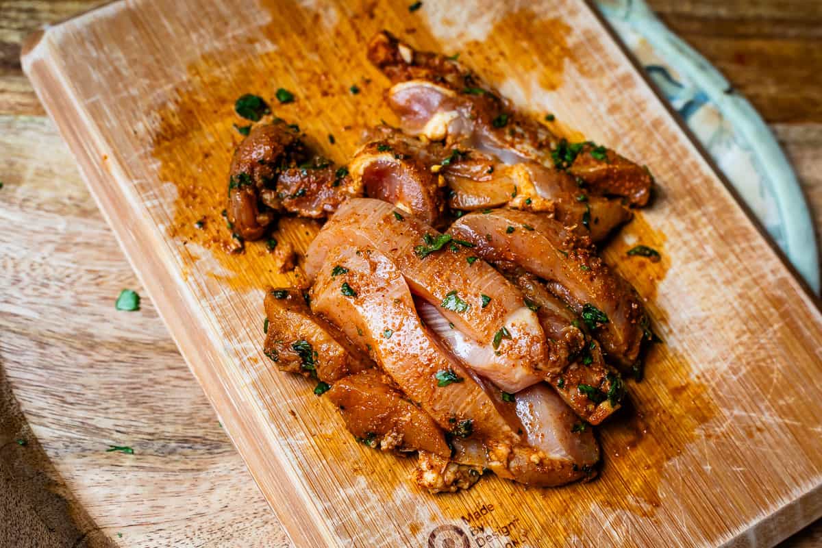 chicken cut into strips and covered in fajita marinade on a wooden cutting board.
