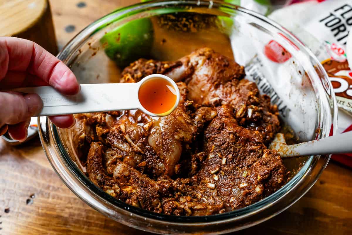 a teaspoon of liquid smoke being poured into the bowl with other marinade ingredients.
