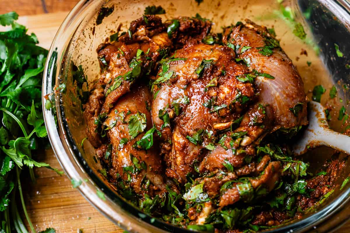 glass bowl with chicken thighs in marinade with cilantro added.