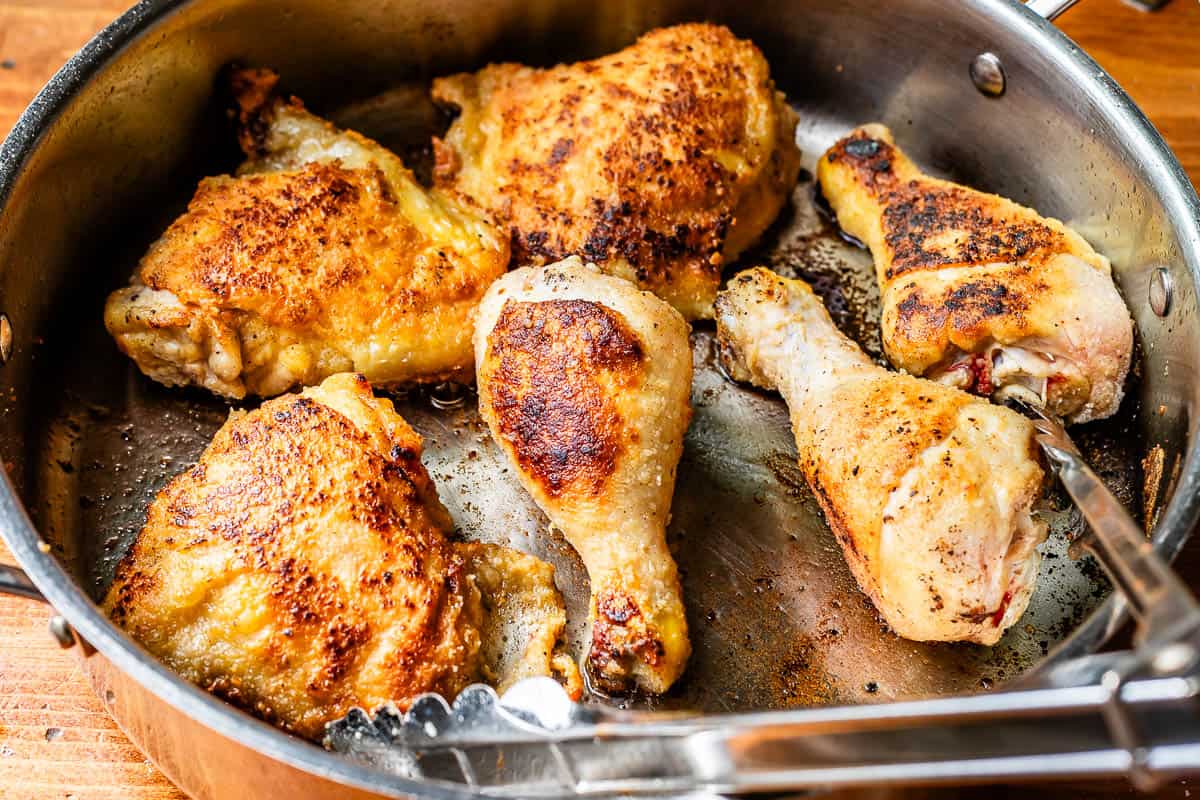 a large skillet with 3 chicken thighs and three drumsticks, all seared on the top.