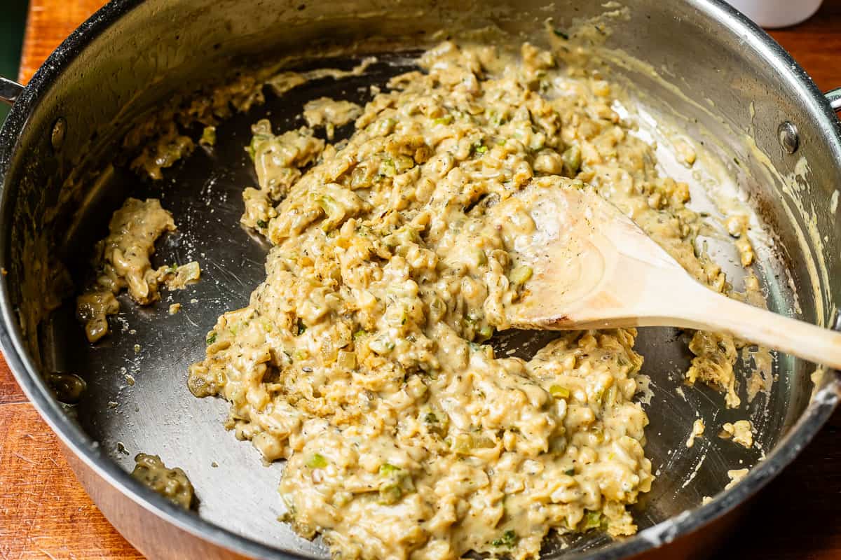 wooden spoon stirring flour and zoup bone broth base covered veggies in metal pan.