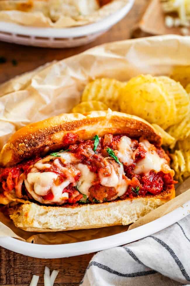 ready to eat meatball sub and potato chips served together on parchment paper in an oval plastic bowl.