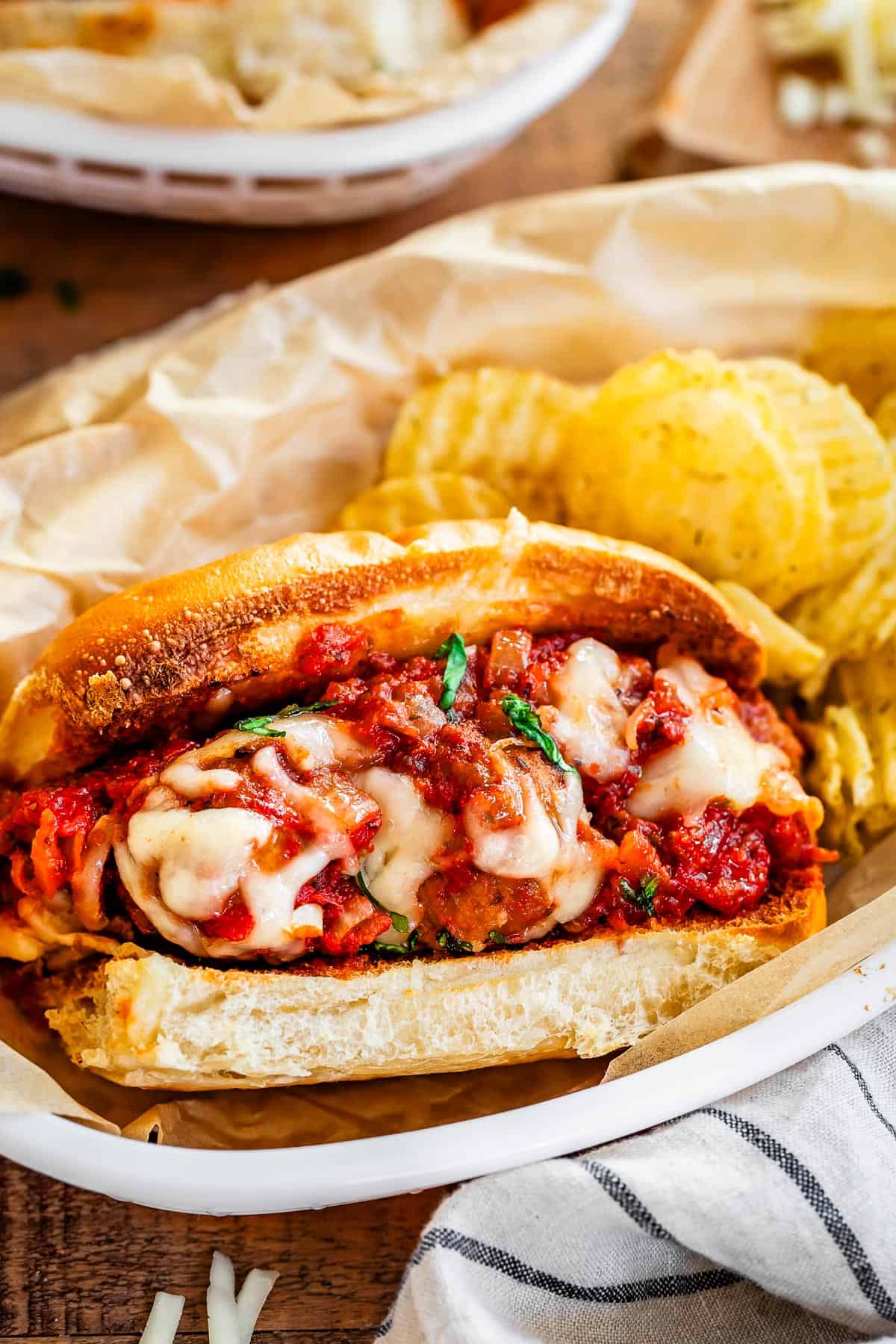 ready to eat meatball sub and potato chips served together on parchment paper in an oval plastic bowl.