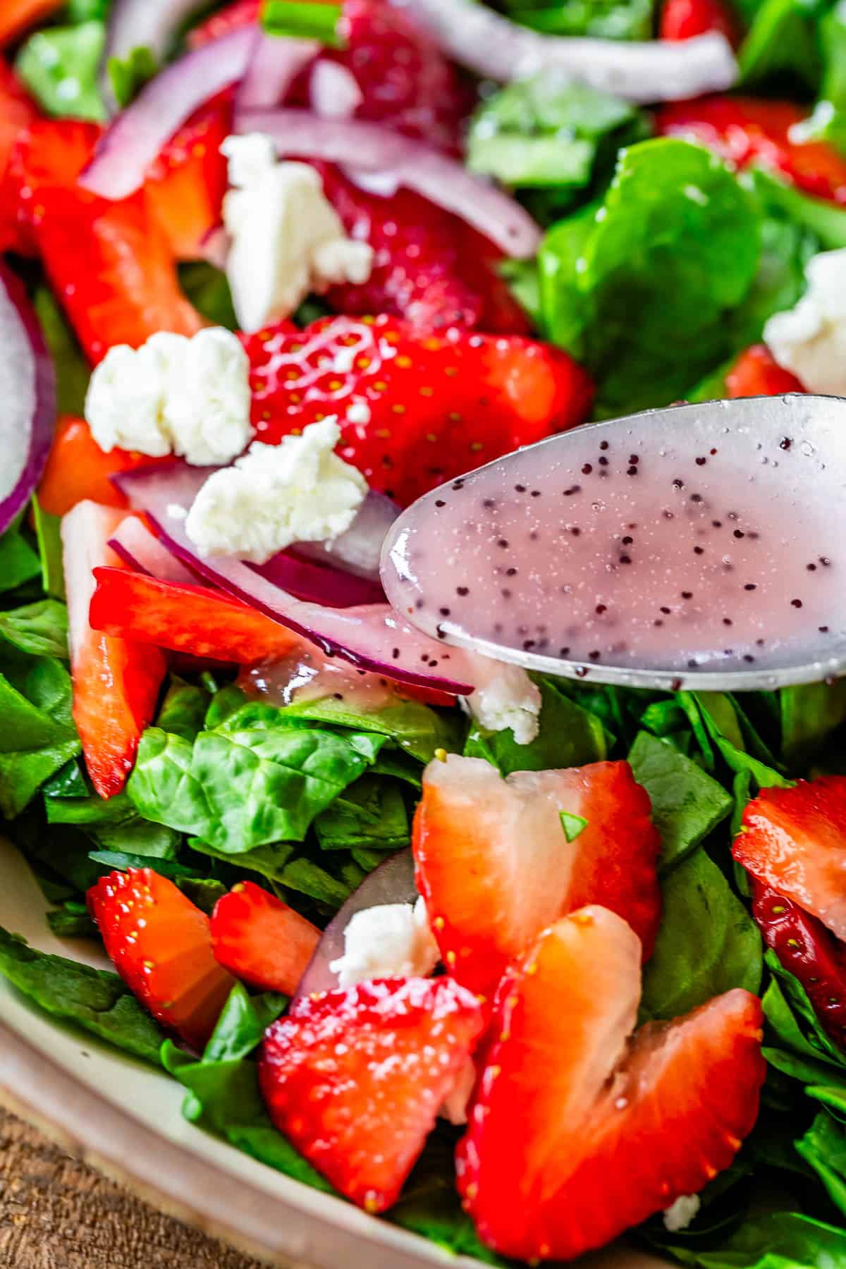 close up of poppyseed dressing being poured from a spoon on top of the ready salad.