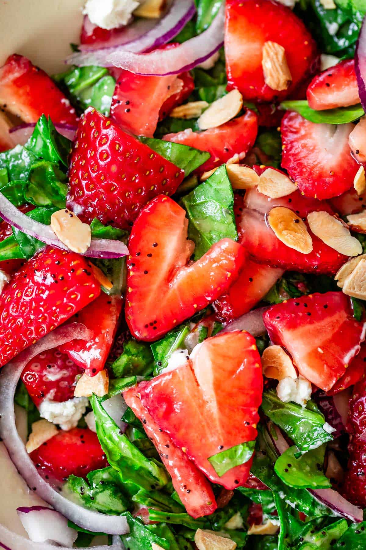close up shot of salad mostly showing strawberries, with some spinach, onions, and almonds.