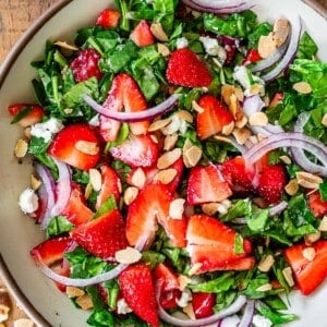 bowl filled with chopped spinach, strawberries, onions, goat cheese, and almonds.