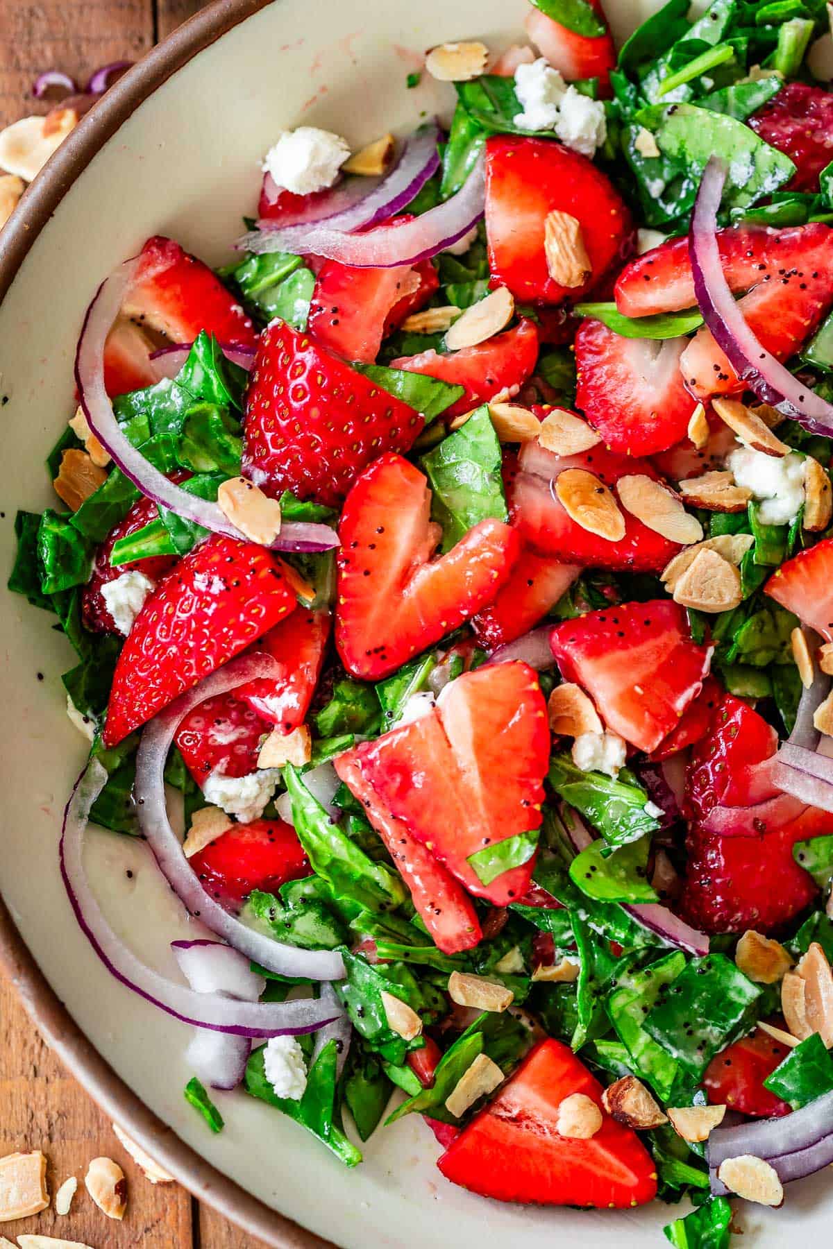 up close on half of a bowl filled with chopped spinach strawberry salad with poppyseed dressing.