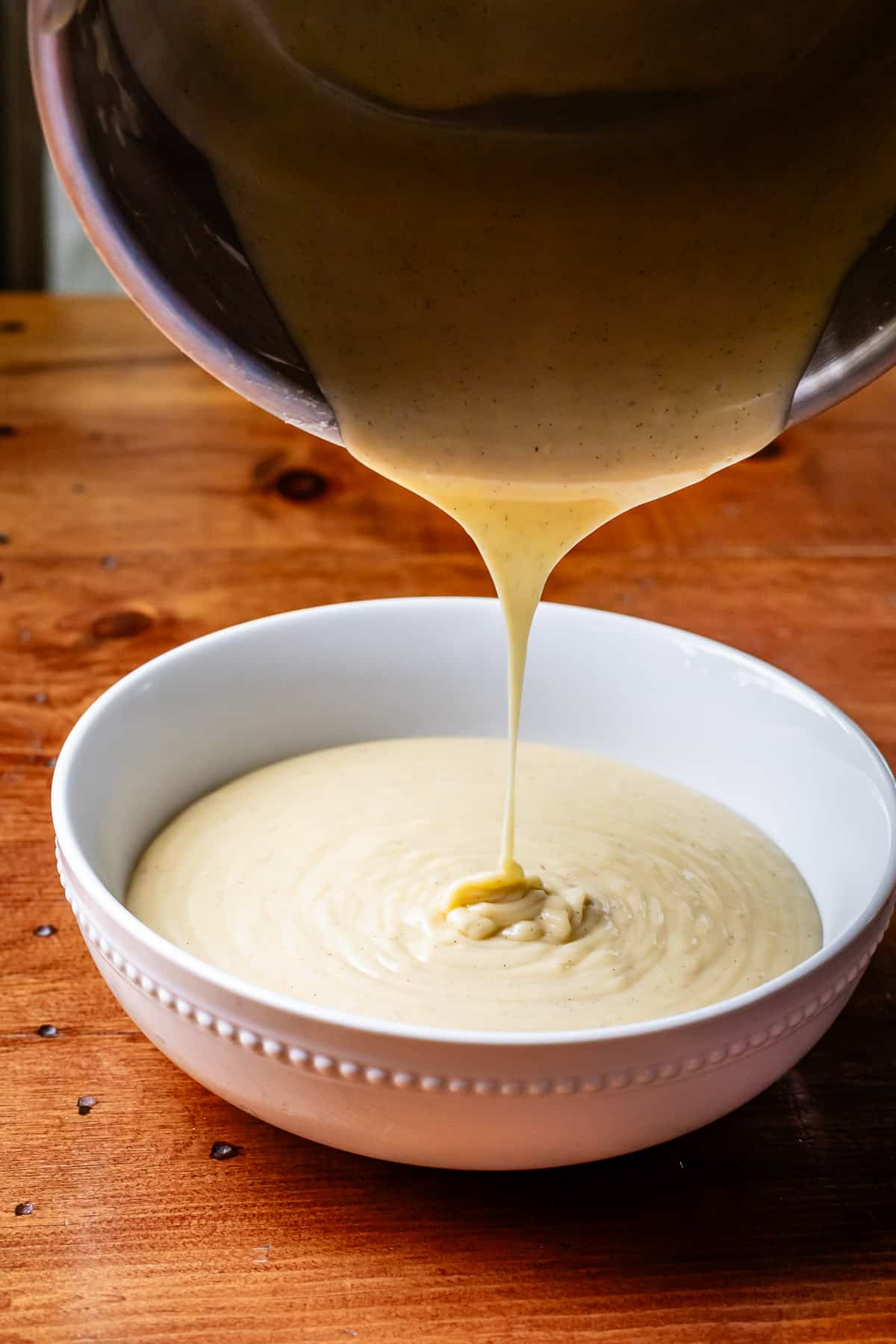 pouring the cooked coconut custard from a metal pot to a ceramic bowl.