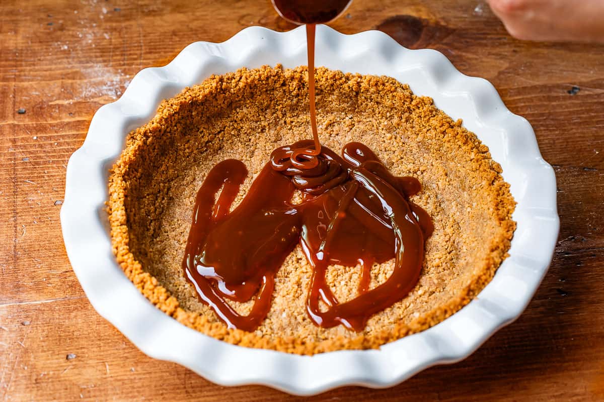 homemade caramel being poured on top of a baked crust in a pie pan.