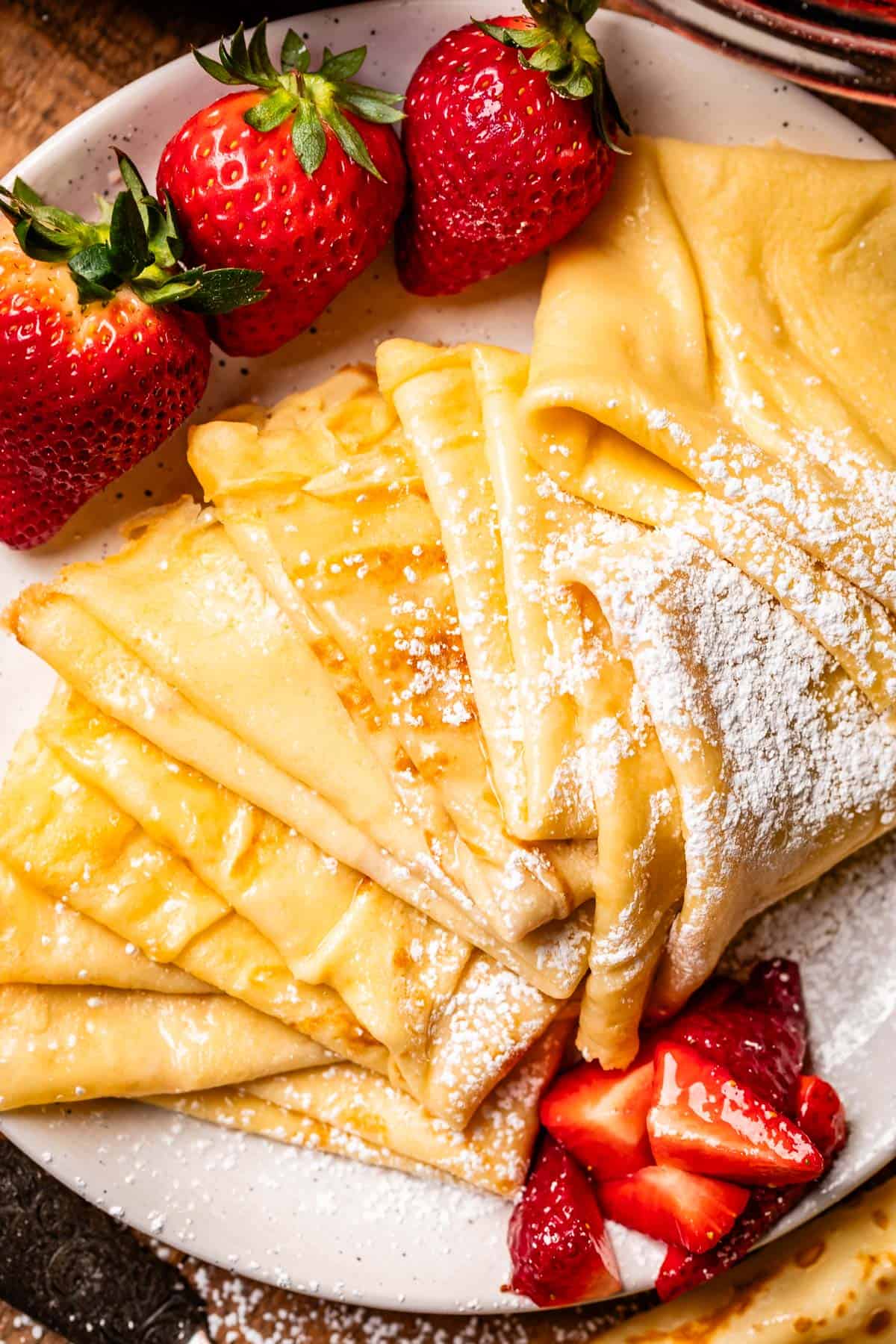 ceramic plate topped with strawberries and multiple crepes folded into quarters.
