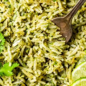 a metal fork digging in to a close up shot of green cilantro lime rice with cilantro garnish.