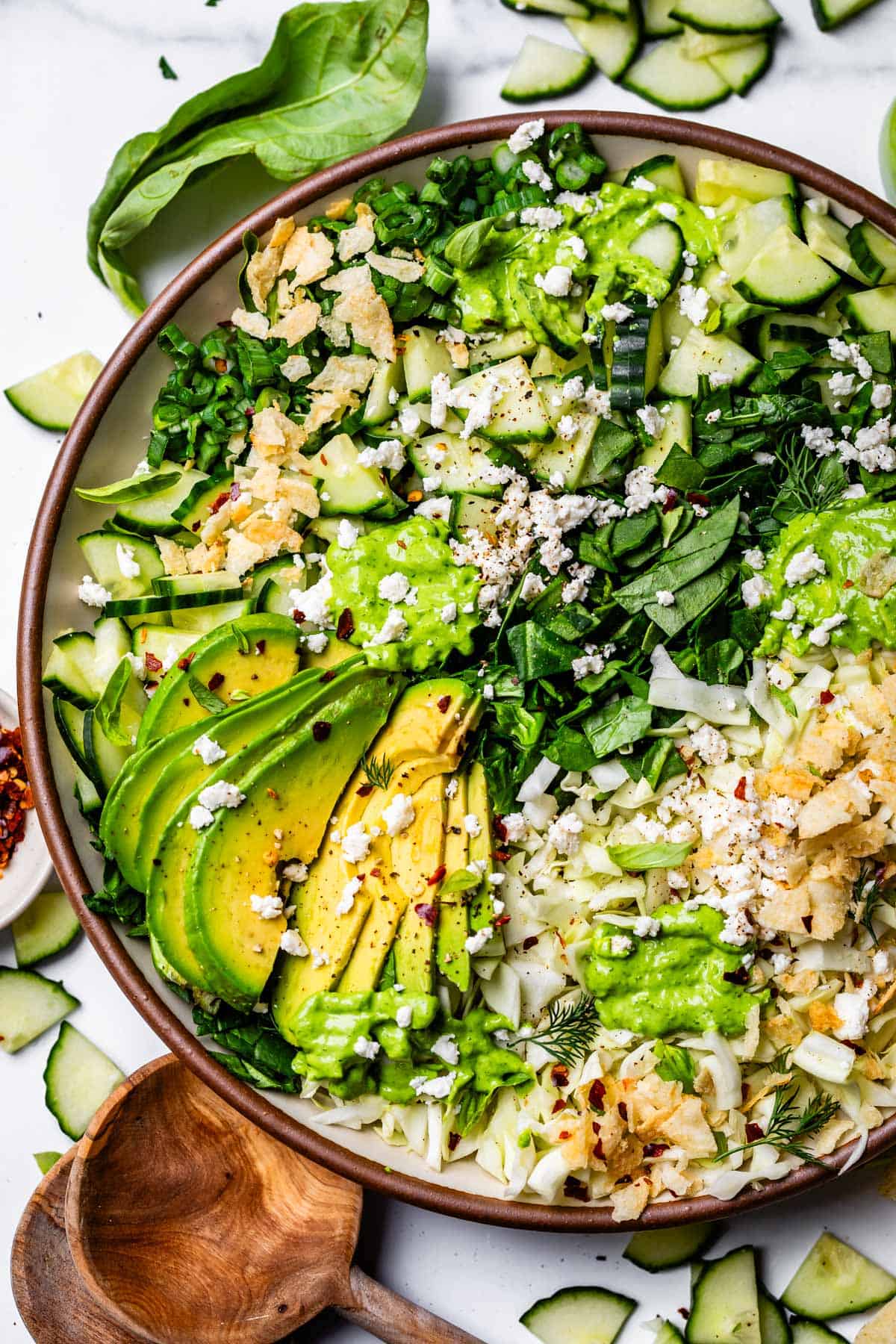chopped salad topped with green goddess dressing on a plate with avocado and chips.