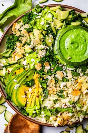 plate full of green goddess salad topped with chips, avocado, and extra dressing.