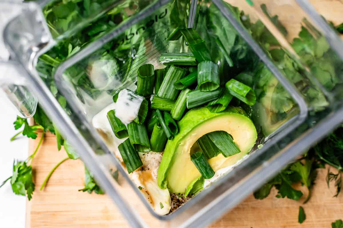 looking into the inside of a blender filled with yogurt, green onion, avocado, and more.
