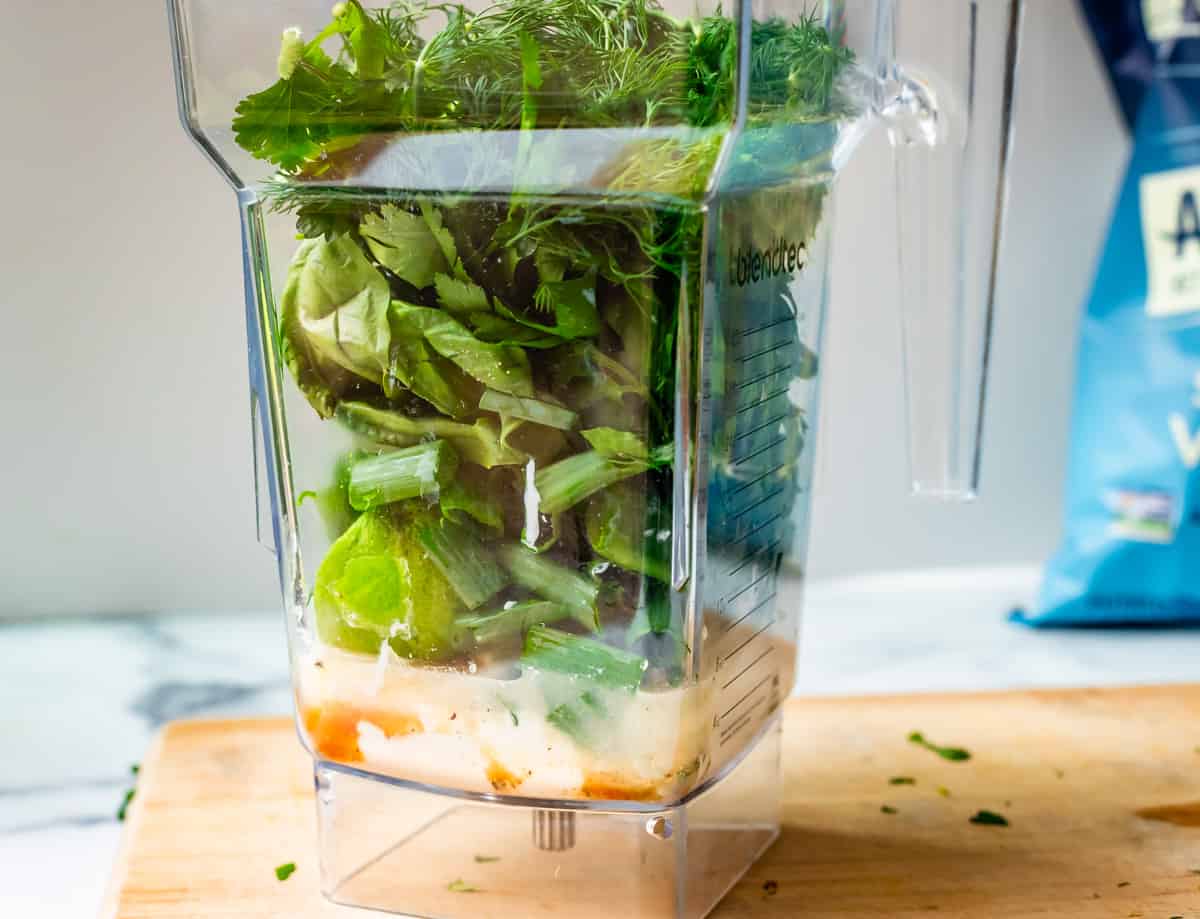 blender with several green goddess ingredients layered inside.