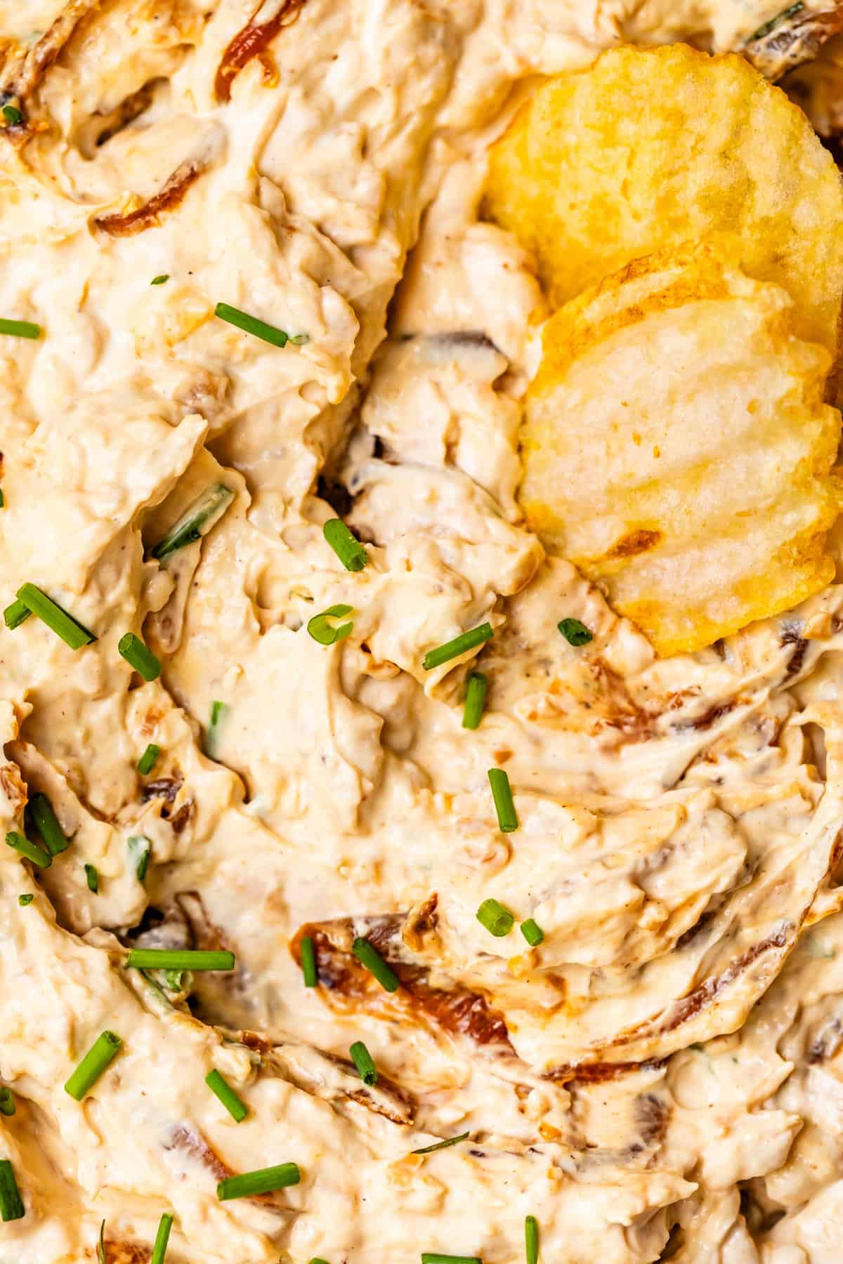 two crinkle cut potato chips nestled into french onion dip with snipped chive garnish.