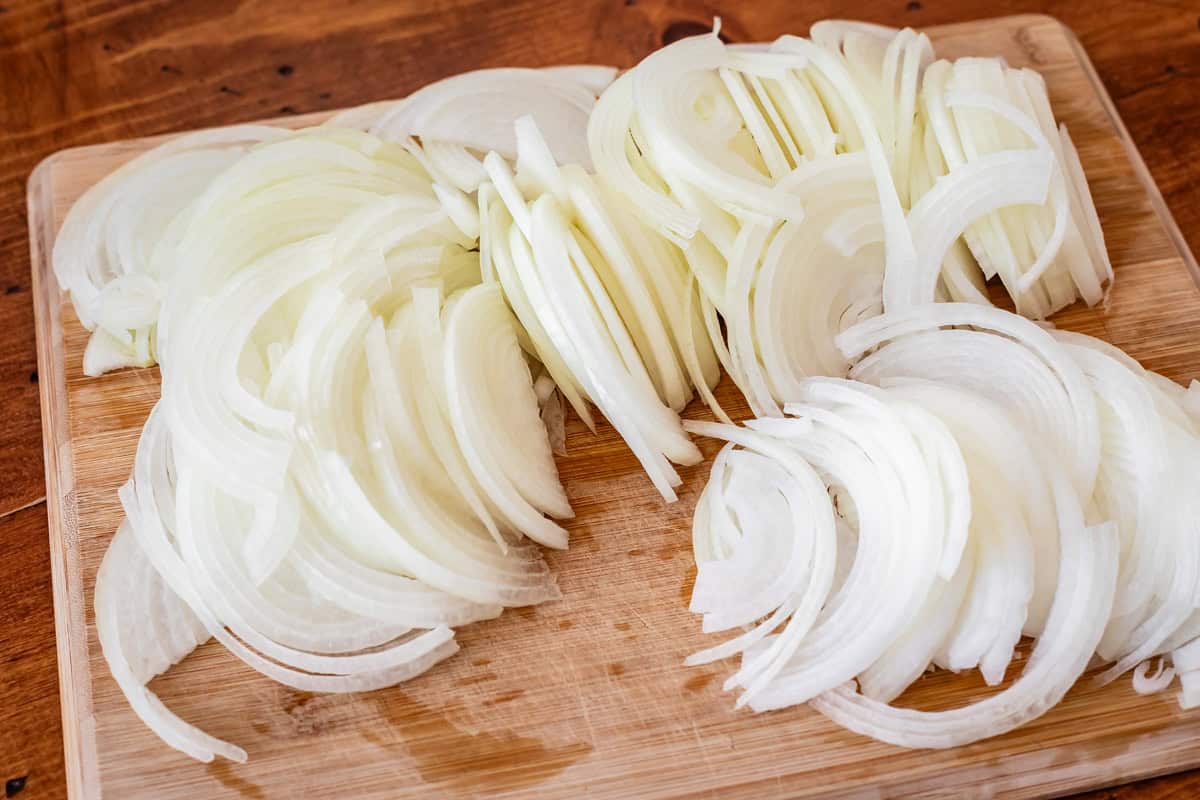 super thinly sliced onions on a wooden cutting board, all ready to be caramelized.