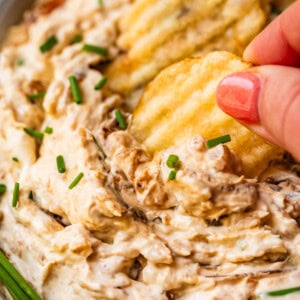 hand pulling crinkle cut potato chip scooping up french onion dip.