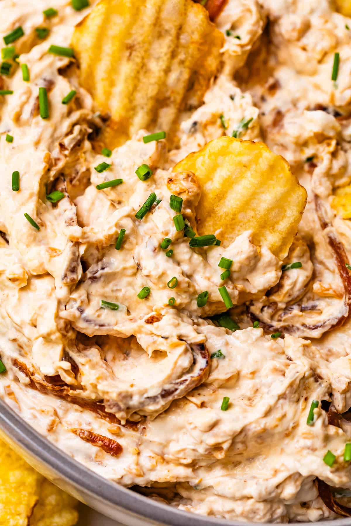 glass bowl of French onion dip with a few crinkle cut potato chips stuck in the top.