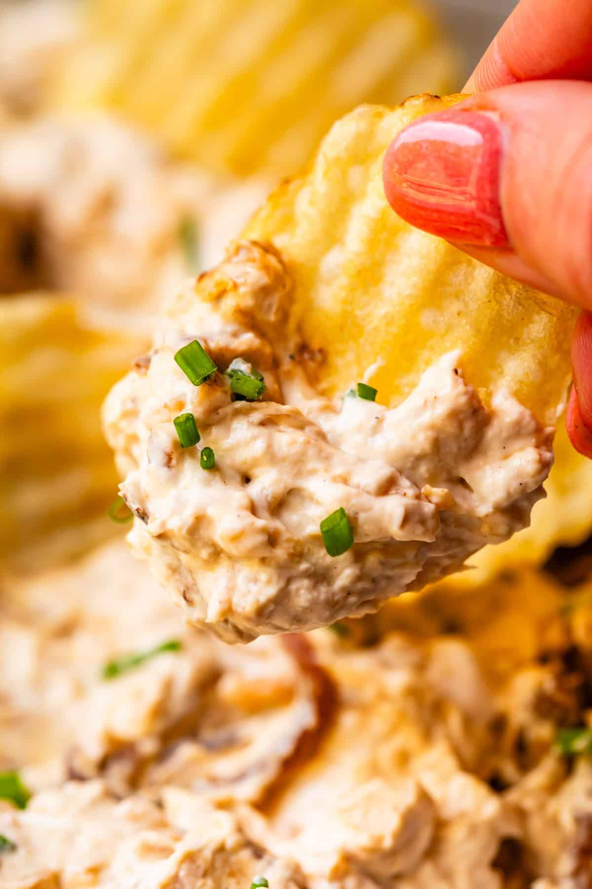 a crinkle cut potato chip laden with French onion dip hovering over the bowl of dip.