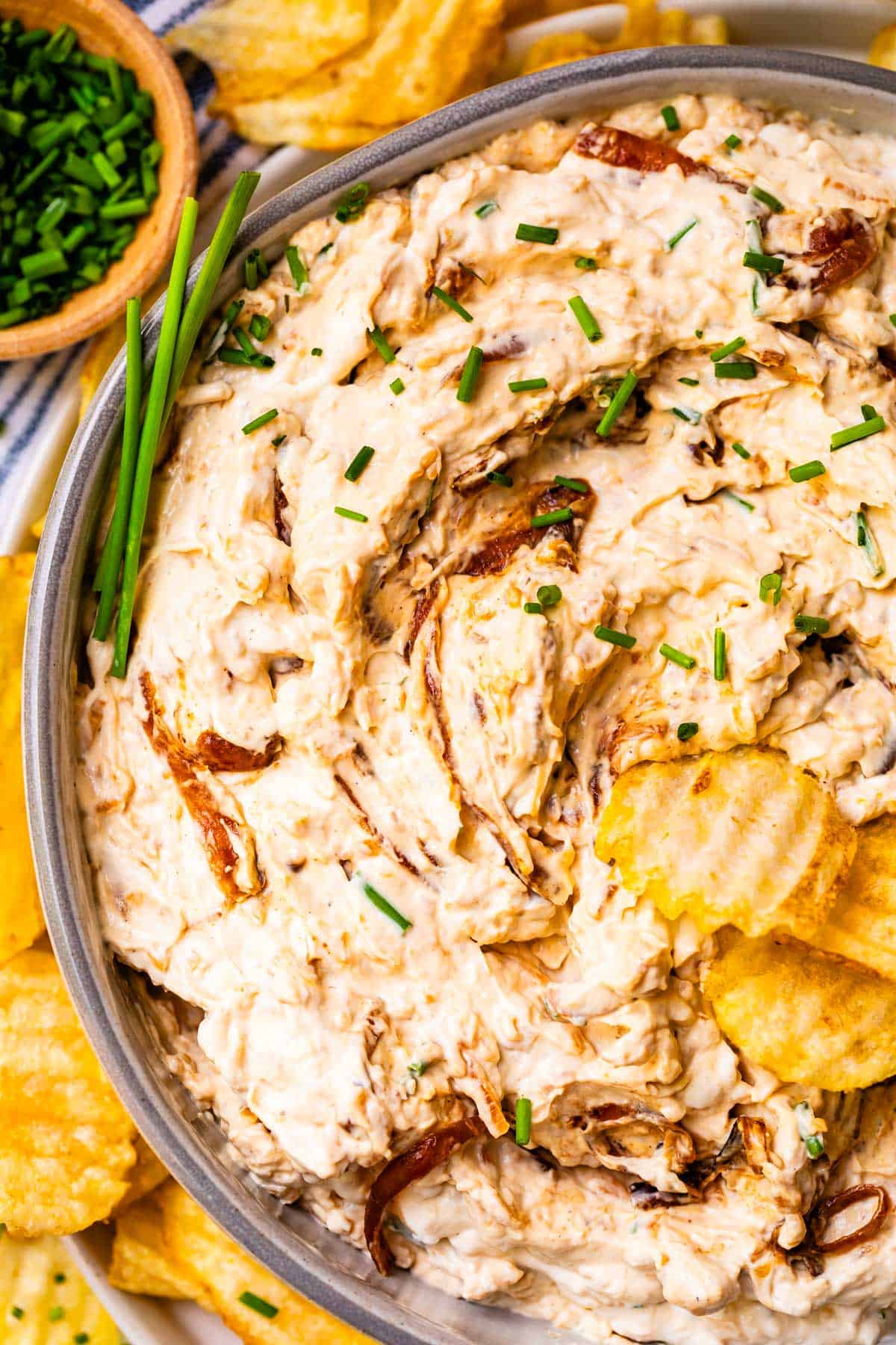 ceramic bowl filled with French onion dip and garnished with snipped chives and potato chips.